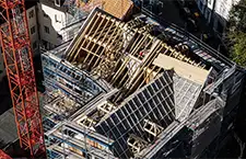Luftaufnahme einer Dachbaustelle in der Altstadt. In der Mitte ist ein großer Dachstuhl im Bau zu sehen, links ein roter Kran.
